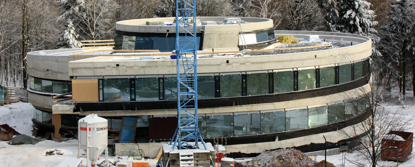 HdA-Gebäude während des Baus, im Schnee - der Betonrohbau mit eingebauten Fenstern ist gut sichtbar. Blick von der Seite auf das im Bau befindliche Haus der Astronomie. Die Fenster sind bereits eingesetzt, aber die Betonstrukturen des Rohbaus sind noch sichtbar.
