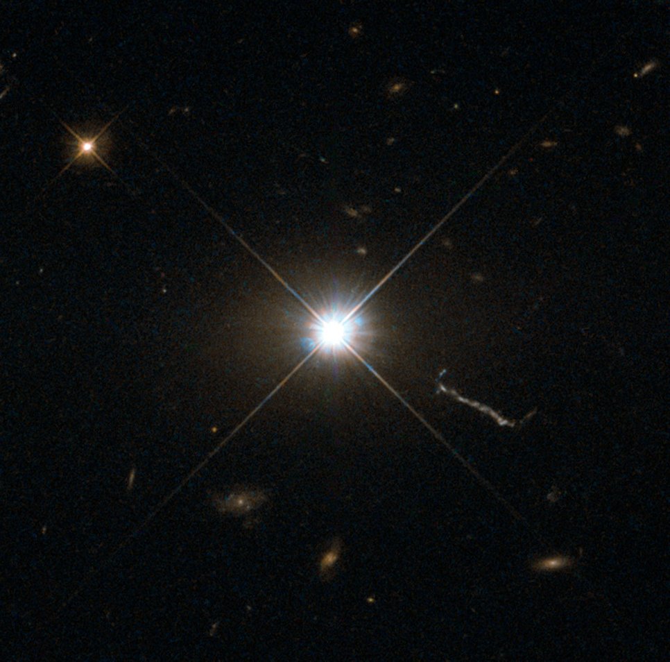 A bright, star-shaped structure together with another star and small, faint galaxies