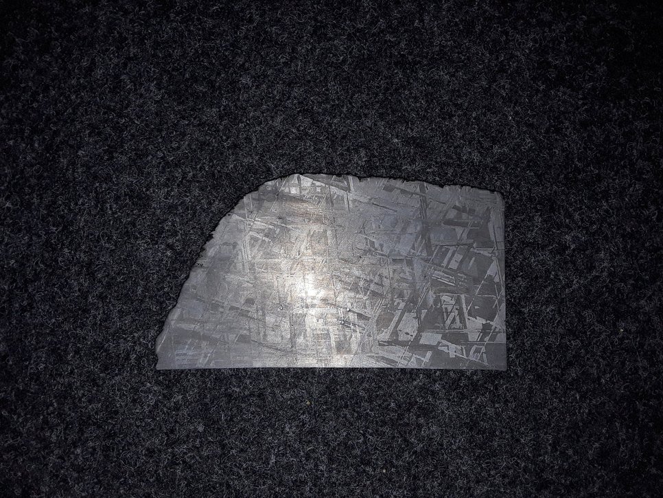 Shiny slice of an iron meteorite with a vertical stripe pattern overlaid by an oblique stripe pattern