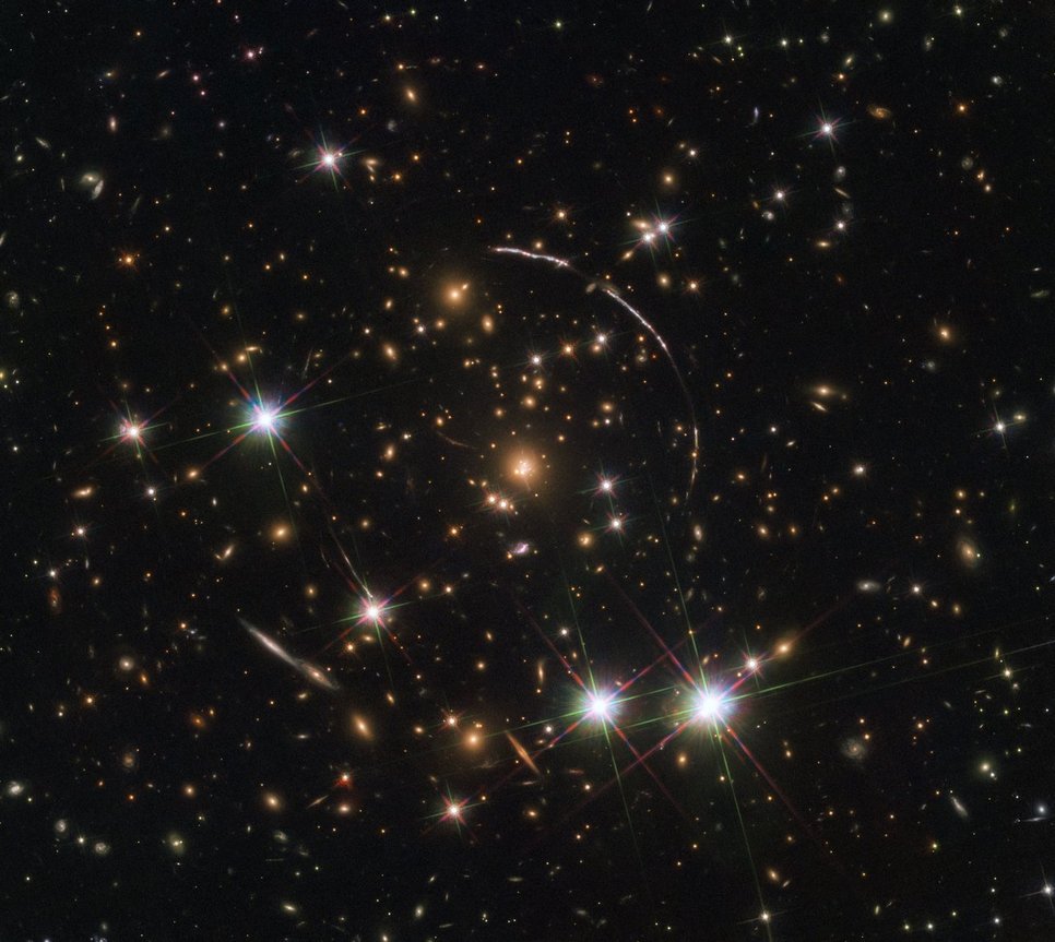 Close-up of a galaxy cluster with four foreground stars surrounded by several segments of a circle