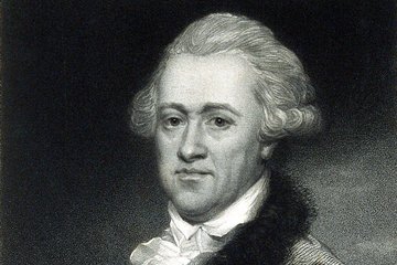 Schwarzbild eines Mannes mit lockigen Haaren hält ein Papier mit einer Zeichnung des Planeten Uranus mit zwei Monden. Er trägt ein weißes Hemd, darüber einen Mantel mit flauschigem Kragen.